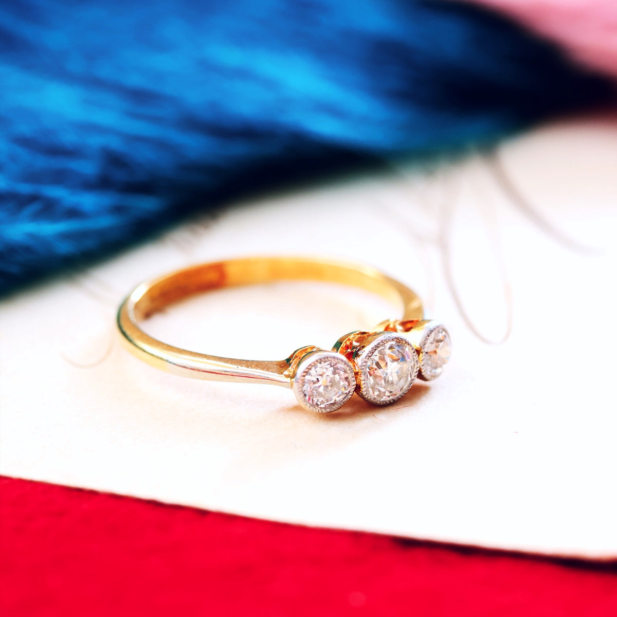 Gold ring with three diamonds on a red and white background