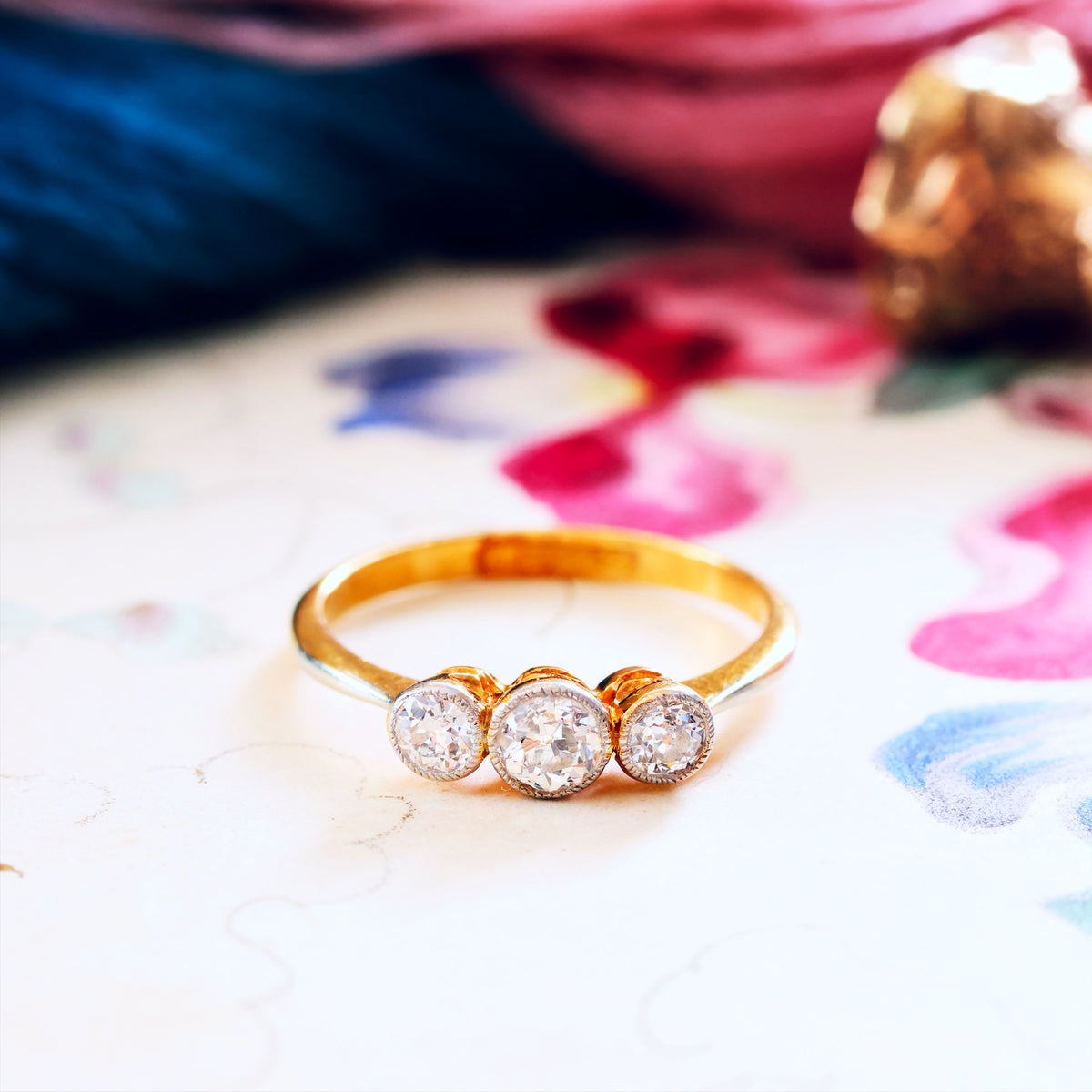 Gold ring with three diamonds on a colorful fabric background