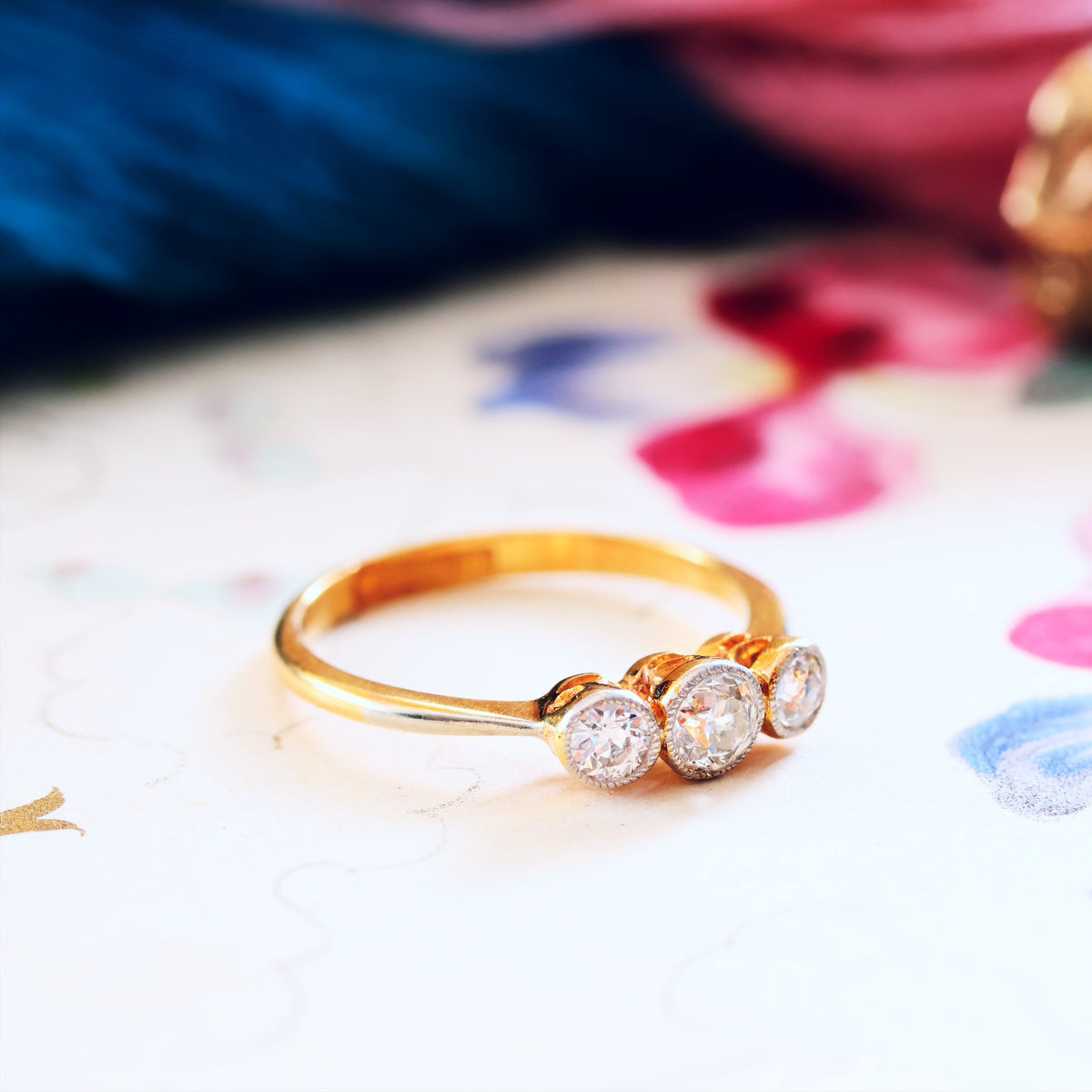 Gold ring with three diamonds on a colourful fabric background